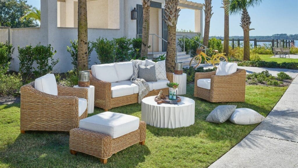 A wicker outdoor set, including a sofa, two arm chairs, a foot stool, and a white table