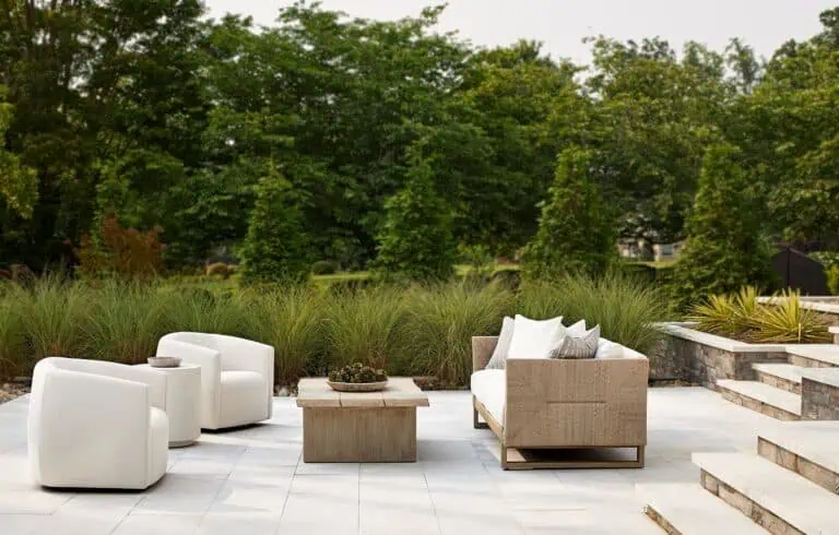 Modern outdoor patio with white chairs, a beige sofa, and a wooden table.