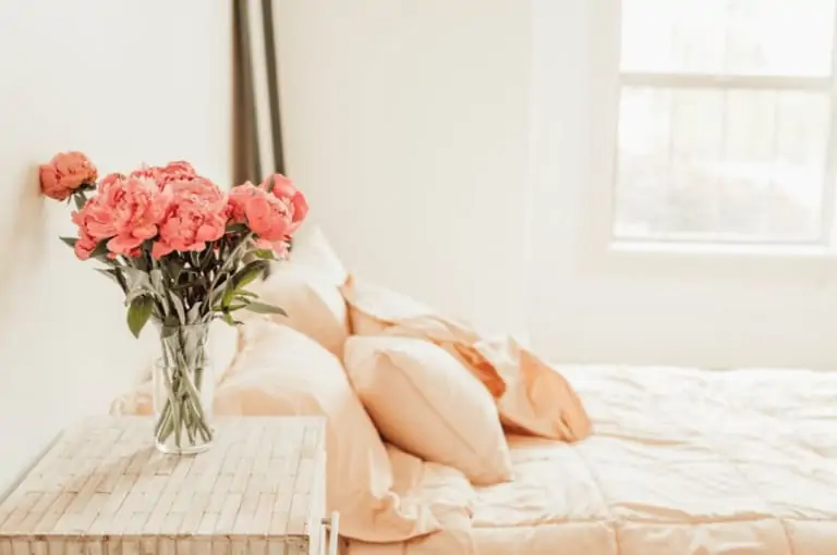 A vase of flowers sits on a nightstand next to a bed