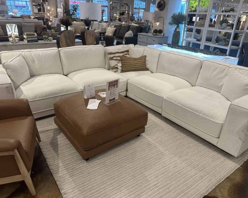 Elegant white sectional sofa with plush cushions, perfect for living rooms. Features a matching ottoman and decorative pillows, ideal for cozy family gatherings.